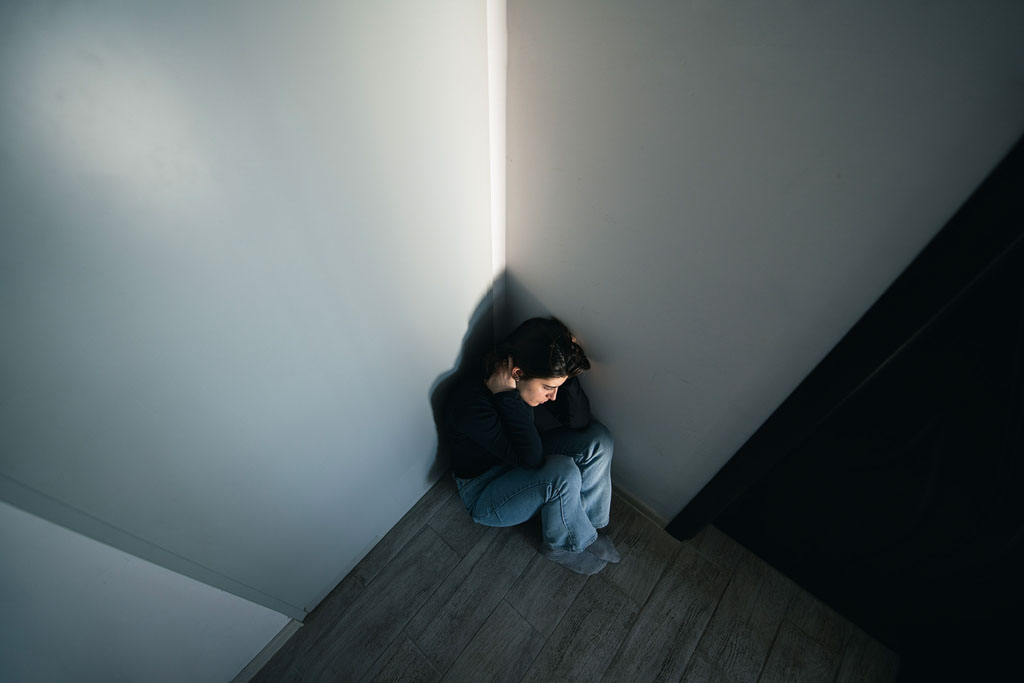 Person in einer Ecke sitzend wirkt niergeschlagen, hilflos und verängstigt